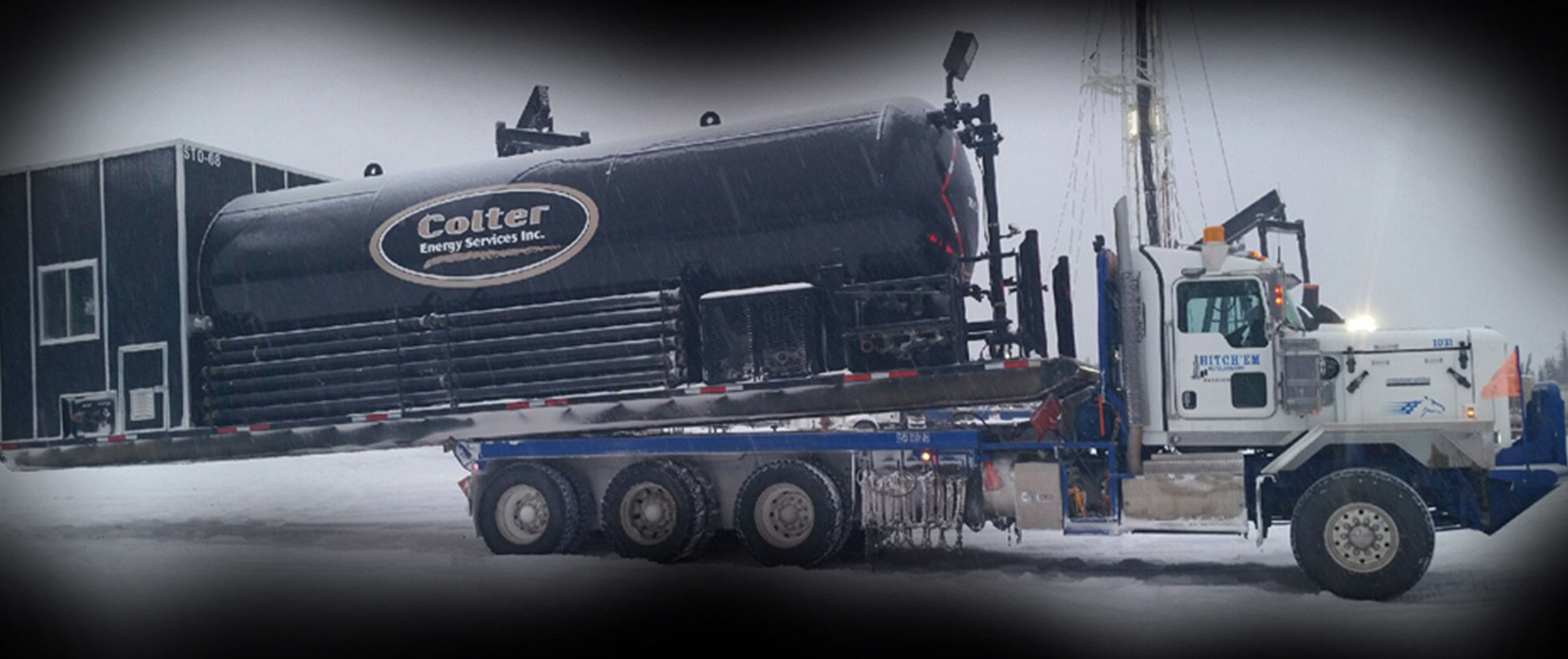Hitch'em bed truck hauling a tank past a Montney drilling rig in winter